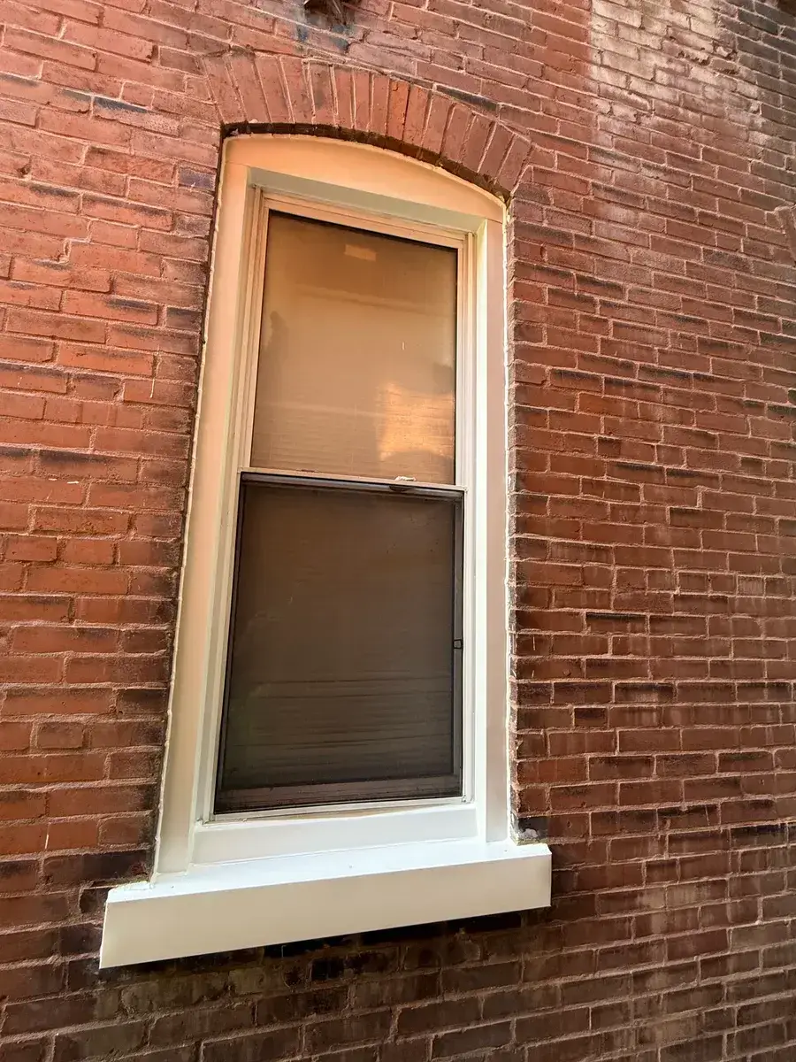 New double-hung window with fresh white capping sealed into the same arched brick opening after installation