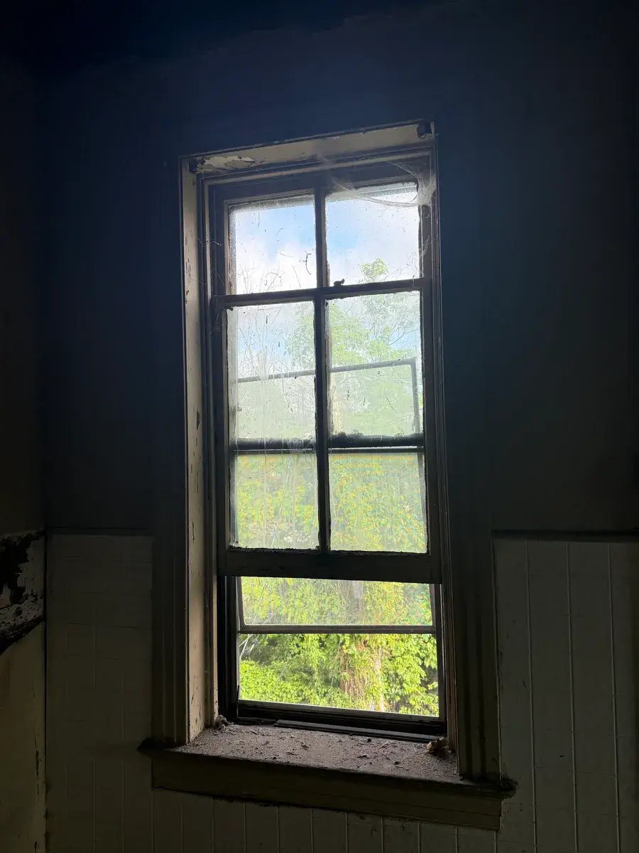 Old wood sash window with grimy divided panes and a deteriorating sill, photographed from inside before replacement